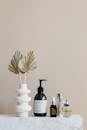 Set of cosmetic supplies near decorative leaves in vase on marble shelf