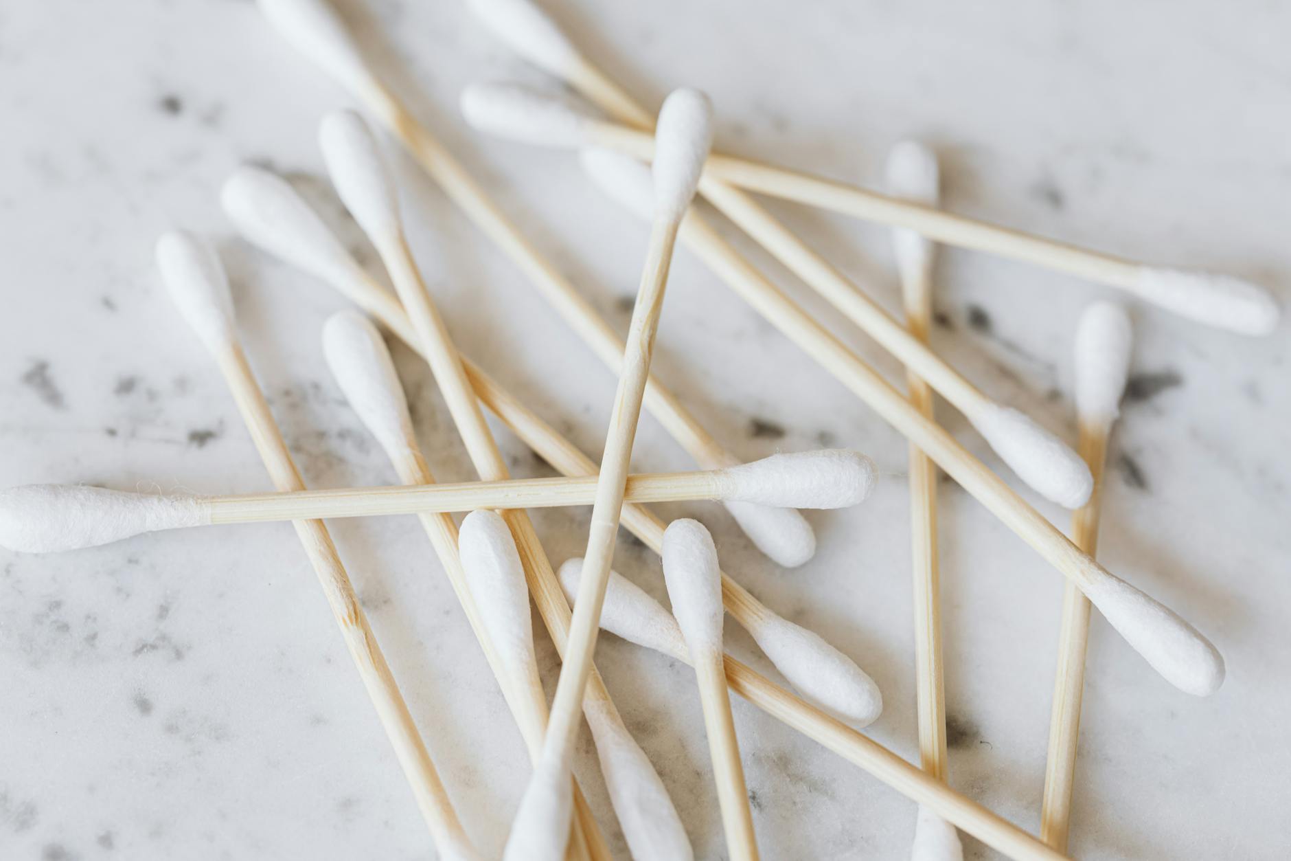 Close-up macro image of multiple bamboo cotton swabs on a white marble surface.