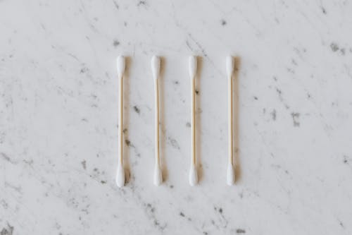 Top view of identical cotton swabs on thin wooden sticks with soft rounded edges on marble surface with tiny spots and gray lines