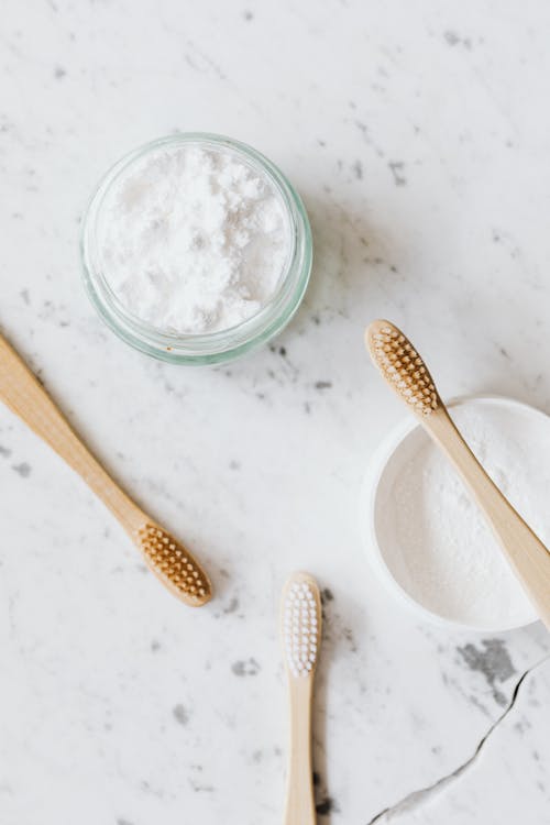 From above of glass and plastic jar with white tooth powder near wooden toothbrushes on marble table with grey lines and crack