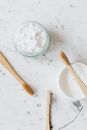 From above of glass and plastic jar with white tooth powder near wooden toothbrushes on marble table with grey lines and crack