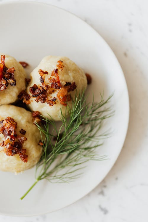 Top view of plate with round big potato dumplings covered with fried bacon bits and served with fresh dill sprig on marble table