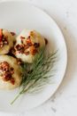 Top view of plate with round big potato dumplings covered with fried bacon bits and served with fresh dill sprig on marble table