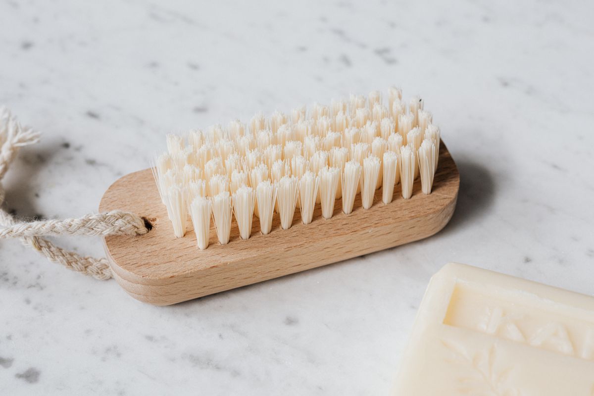 Wooden cleaning brush with pale bristles beside an unlabelled soap bar on marble