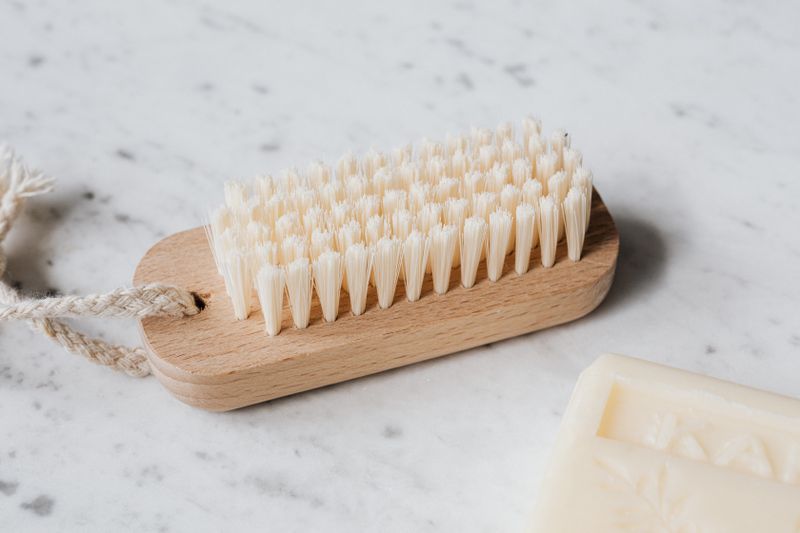 Wooden cleaning brush with pale bristles beside an unlabelled soap bar on marble