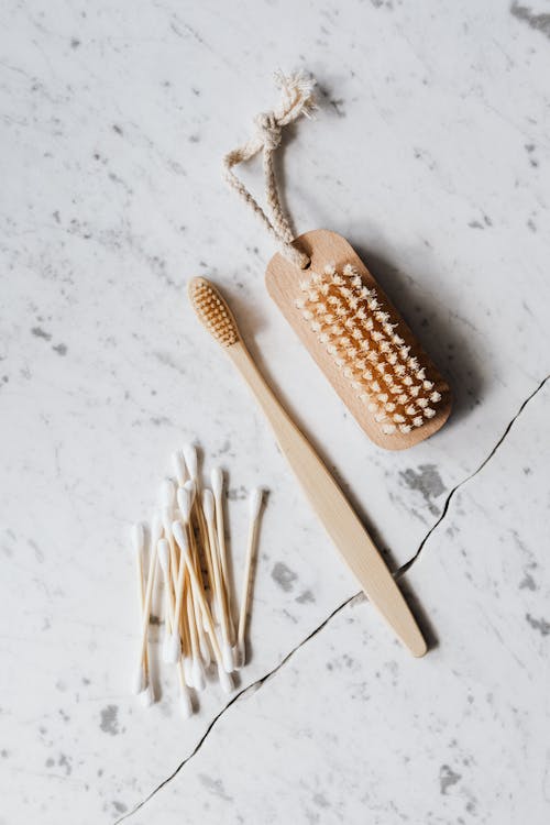 Top view layout of wooden cleaning brush and cotton swab placed on marble surface near wooden toothbrush on line chop