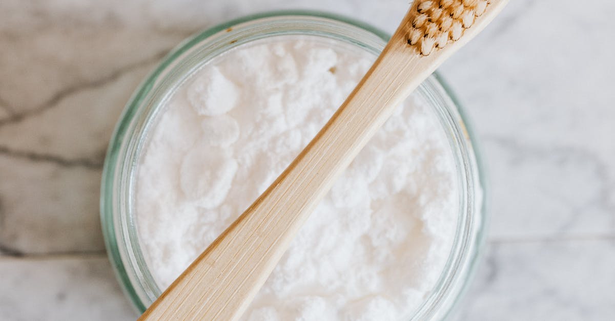 Top view of wooden toothbrush placed over glass jar of tooth powder on marble surface