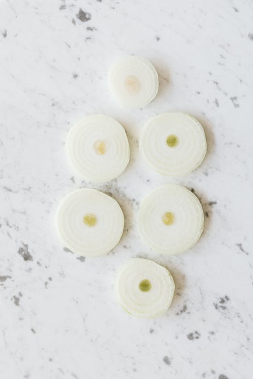 Top view of cut into ring fresh peeled organic yellow onion placed on clean white marble surface before cooking process
