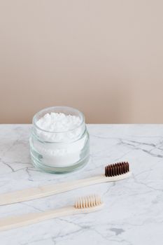 Zero waste concept reusable glass jar with organic toothpaste and wooden environmentally friendly toothbrushes placed on marble tabletop against beige wall