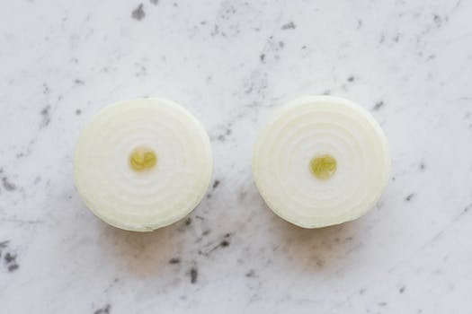 Top view of raw peeled aromatic onion cut into halves and placed on white marble tabletop