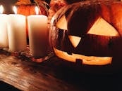 Spooky carved Jack o lantern pumpkin placed on wooden table near burning candles during Halloween party