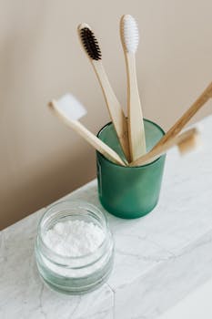 Sustainable bamboo toothbrushes in a glass container with natural toothpowder in a jar on a marble surface.