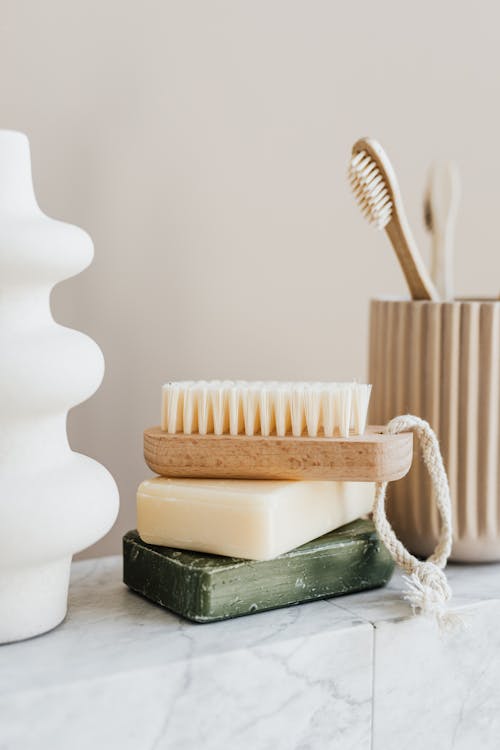 Free Sustainable consumption concept collection of organic cruelty free soaps with wooden body brush near bamboo sustainable toothbrushes and ceramic white vase on marble tabletop in minimalist bathroom Stock Photo