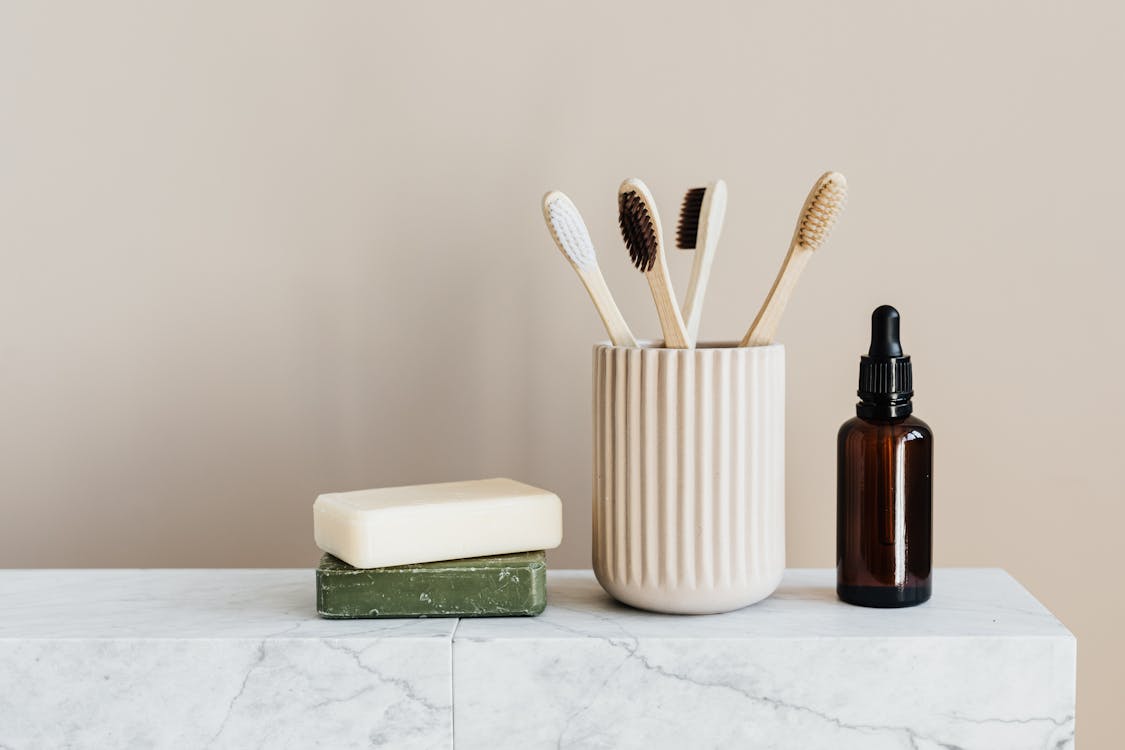 Free Collection of organic soaps and bamboo toothbrushes in ceramic minimalism style holder placed near renewable glass bottle with essential oil on white marble tabletop against beige wall Stock Photo