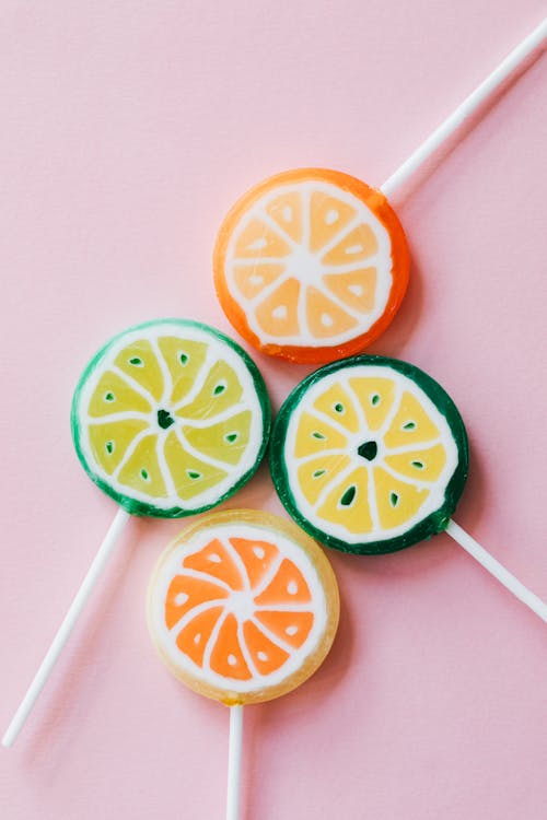 Free From above of round shaped colorful candies similar to citrus fruits on plastic sticks on pink surface Stock Photo