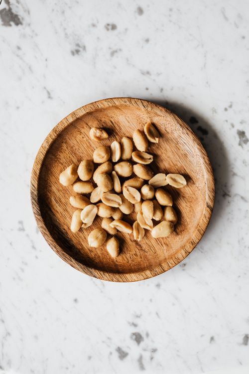 Free Overhead shot of peeled peanuts served on a rustic wooden plate against a marble background. Stock Photo