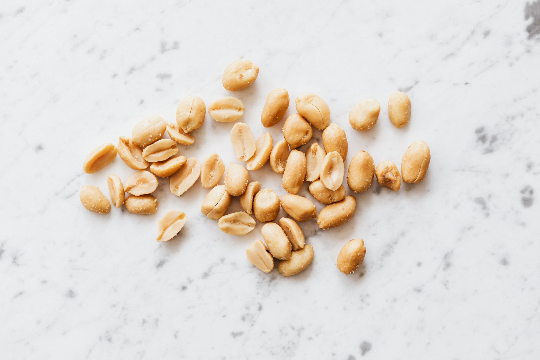 A close-up image of salted peanuts scattered on a marble surface, showing texture and details.
