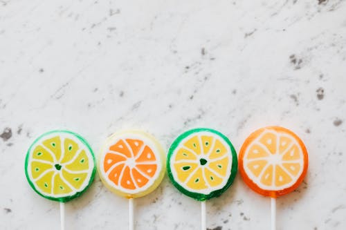 From above of bright round shaped candies with creative decoration inside on thin plastic sticks on marble surface