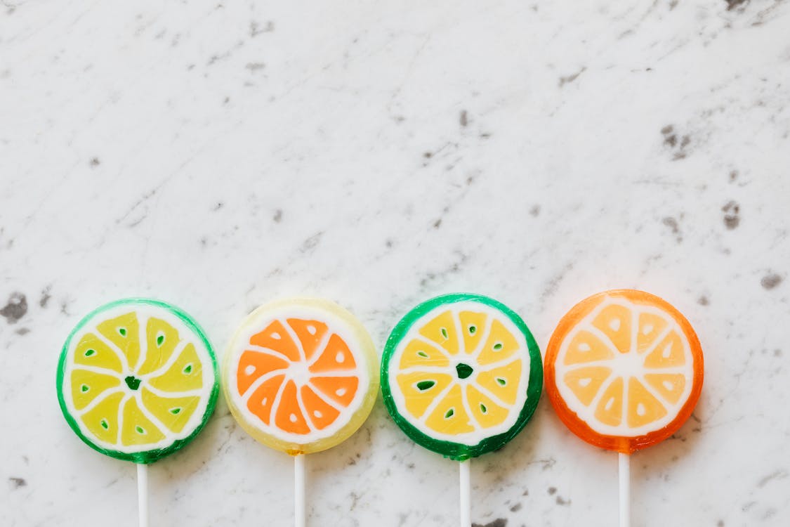 From above of bright round shaped candies with creative decoration inside on thin plastic sticks on marble surface