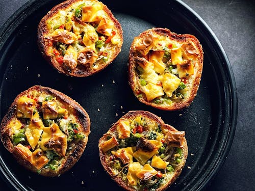 Top view composition of crispy tasty mini bread pizzas with vegetables and cheese served on black tray