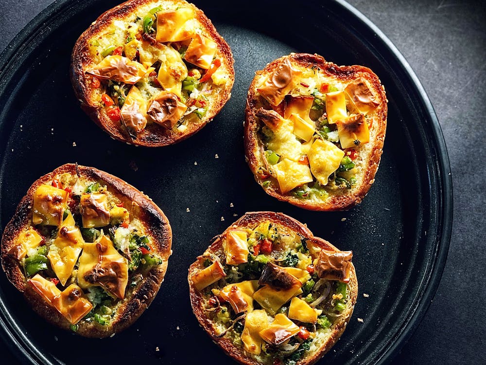 Top view composition of crispy tasty mini bread pizzas with vegetables and cheese served on black tray