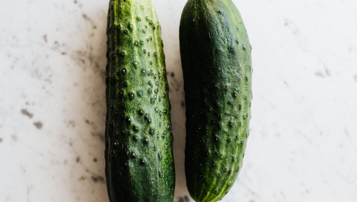 Two fresh whole cucumbers on a white marble surface