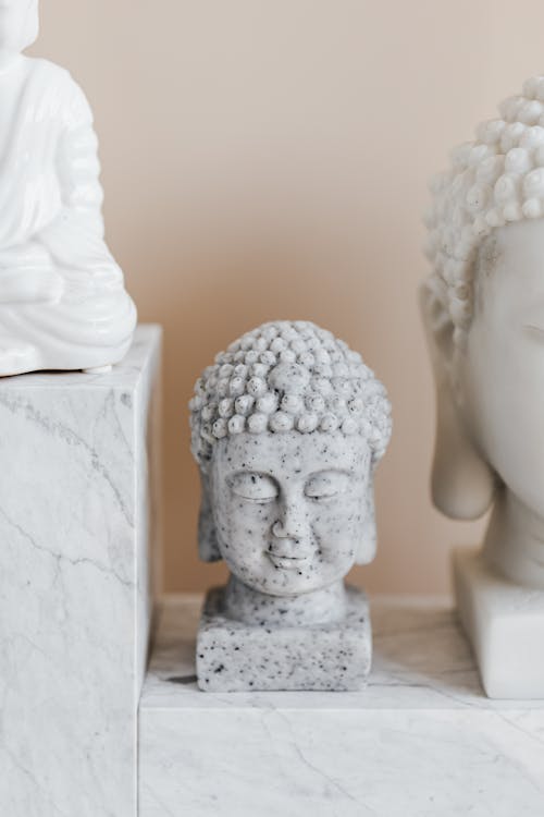 Small bust of Buddha with closed eyes and bubbly headdress made of speckled marble near Asian sculpture collection on beige background