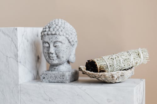 Bust of Buddha and dry sage bundle on marble surface