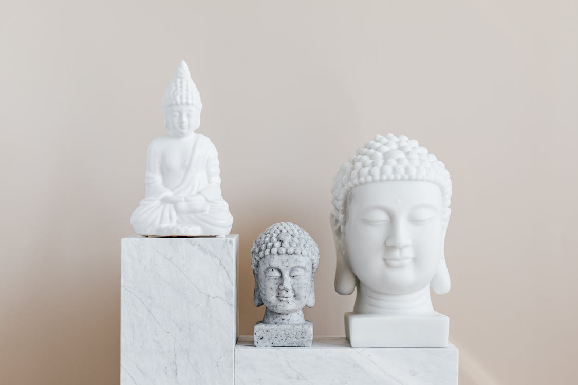 Collection of Asian busts and statue of Buddha made of white and gray stone with smooth surface on marble pedestal