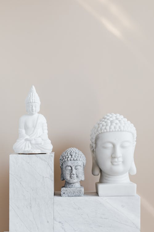 Set of various gypsum and stone Buddha sculptures placed on white marble shelf against beige wall as home decoration element and religion symbol