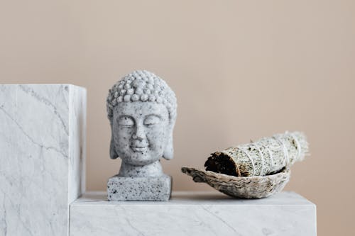 Free Stone Buddha and sage incense bundle in bowl on marble shelf Stock Photo