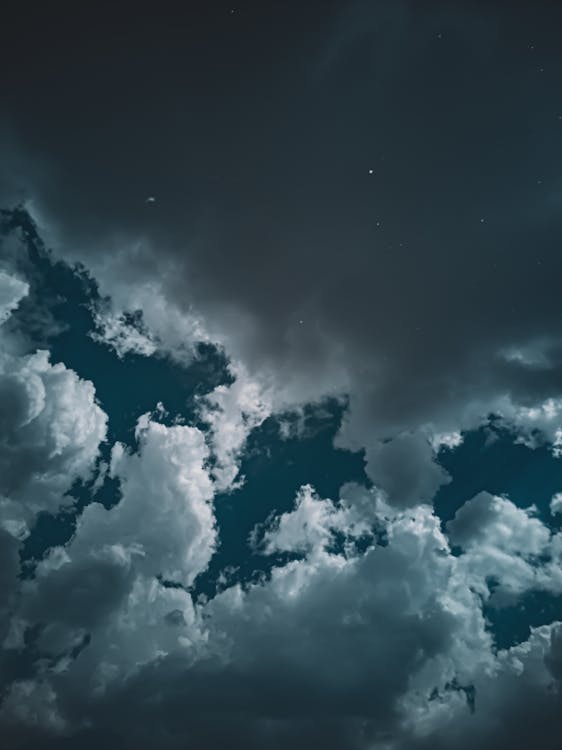 From below of dark blue sky with gray and white fluffy clouds at night