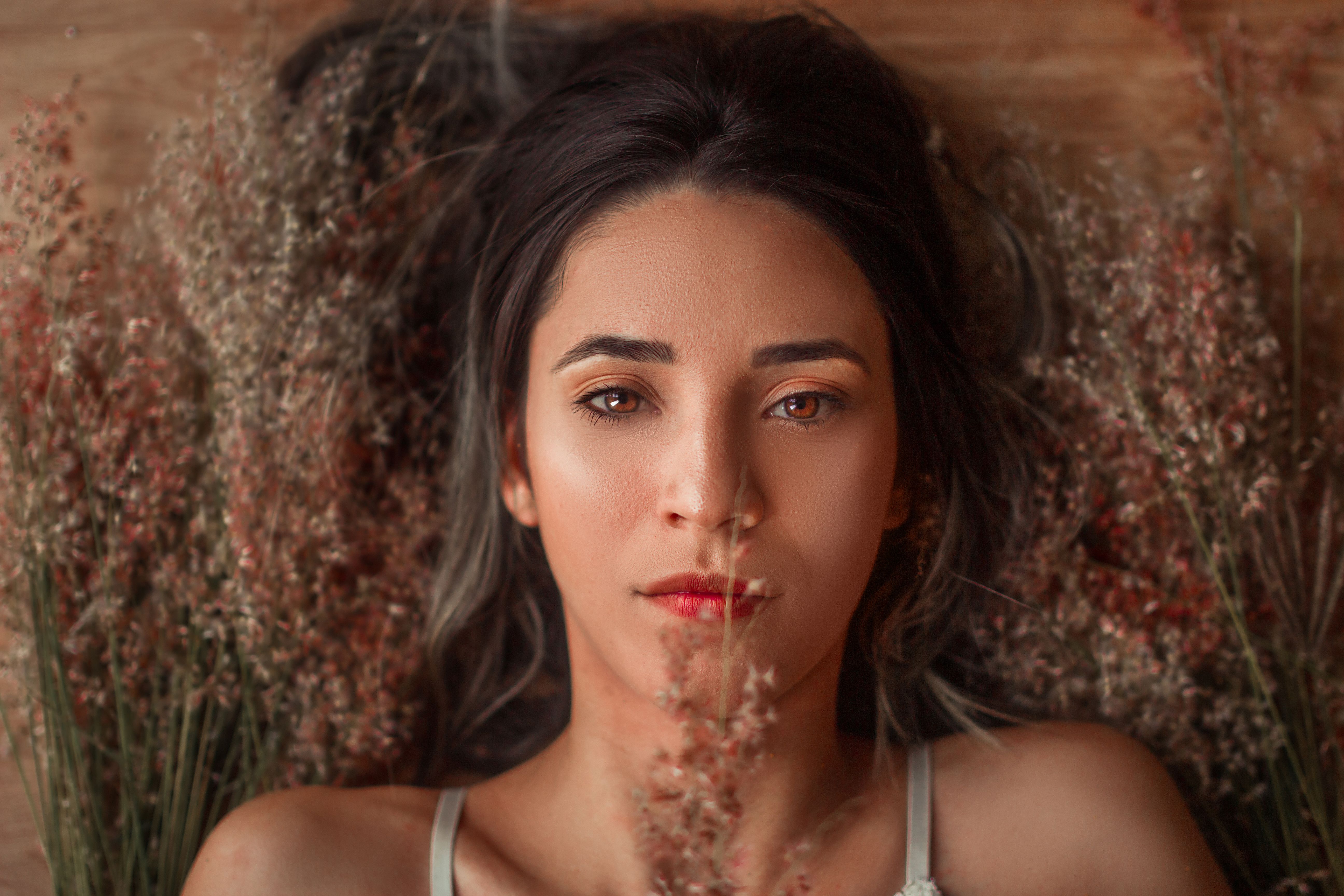 Beautiful woman with brown eyes lying among dried flowers, creating a serene and natural portrait.