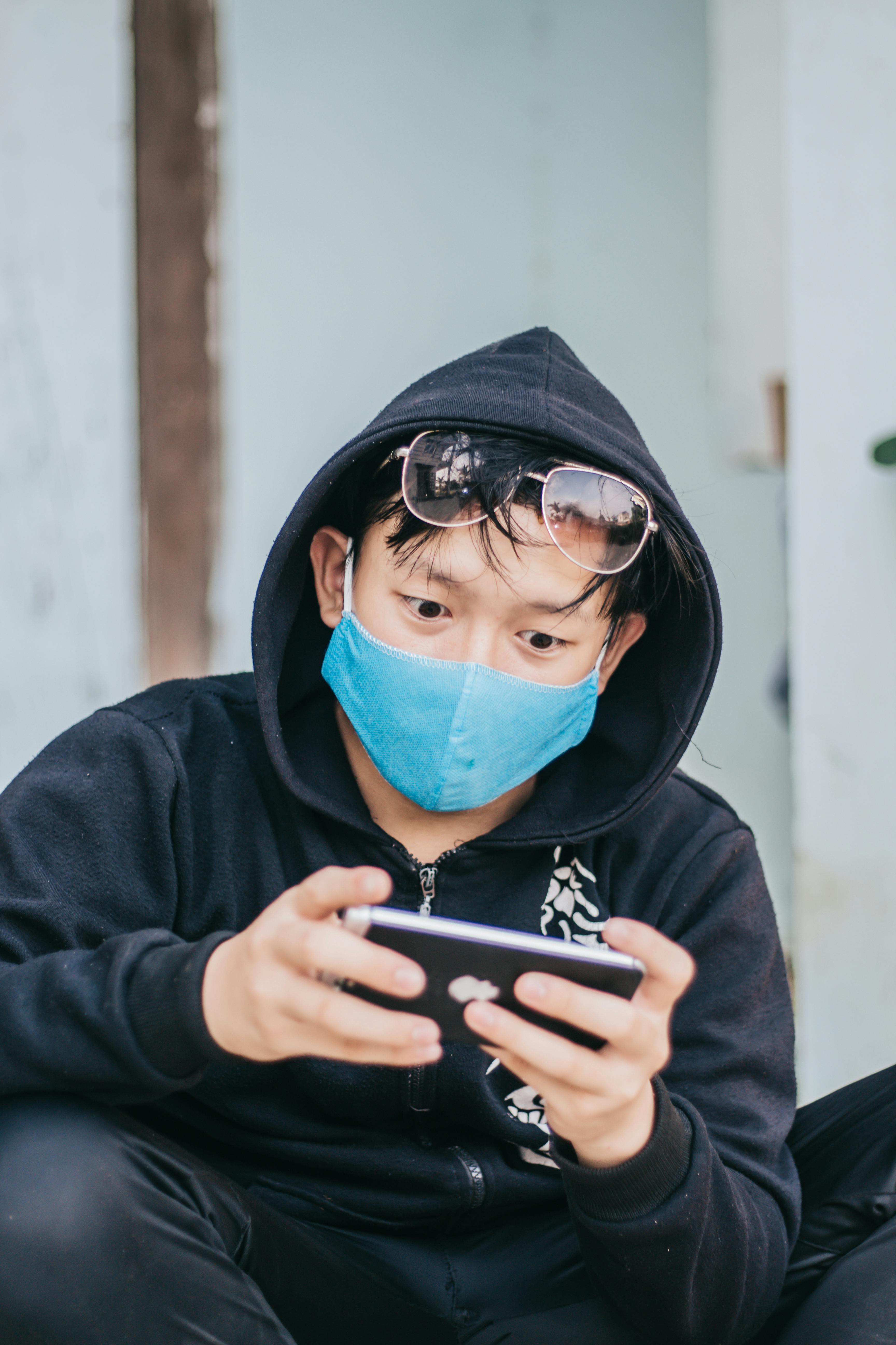 Person Wearing Black Hoodie and Blue Face Mask While Using Smartphone ·  Free Stock Photo