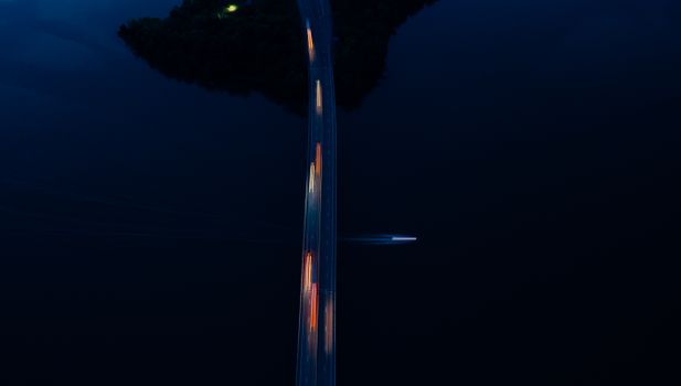 Picturesque aerial view of cars riding on bridge road over river with floating boat at night