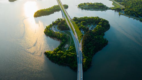 Free Picturesque drone view of road bridge going through green forests and crossing calm lake at sunset Stock Photo