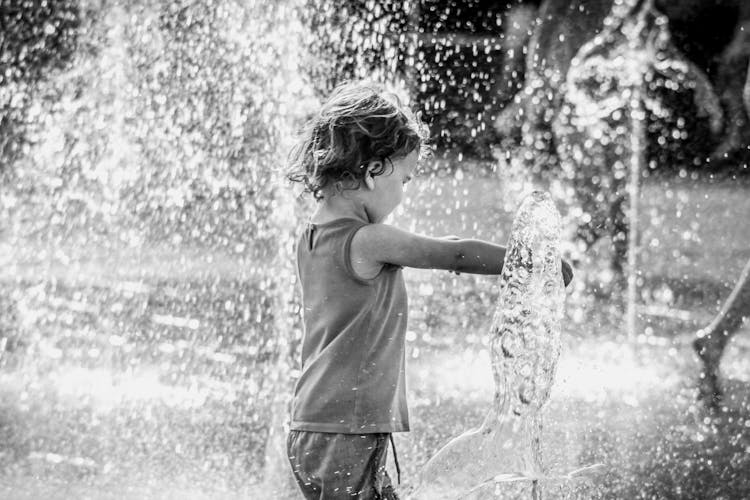 Grayscale Photo Of Child Playing In Water Fountain