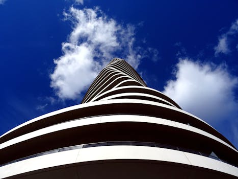 现代摩天大楼拥有弧形立面和玻璃窗，在蓝天的映衬下飘着云朵