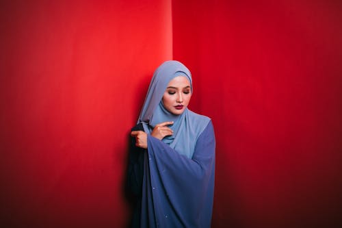 Woman in Blue Hijab Standing Beside Red Wall