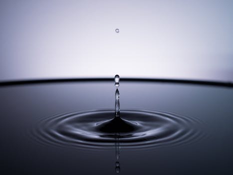 Close-up of a single water droplet creating ripples on a calm surface, captured in a minimalist style.