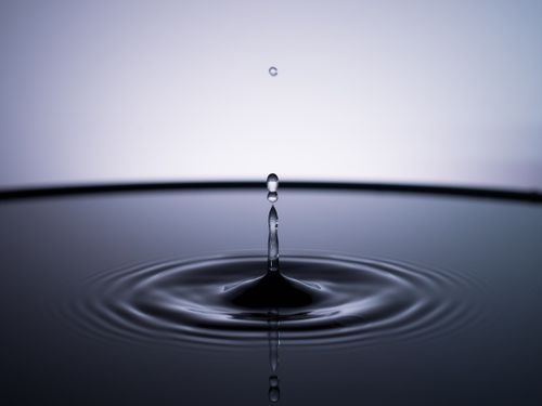 Free Close-up of a single water droplet creating ripples on a calm surface, captured in a minimalist style. Stock Photo