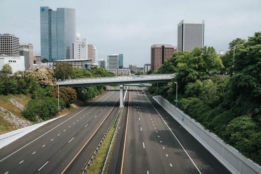 Contemporary cityscape featuring an empty highway flanked by skyscrapers and lush greenery.