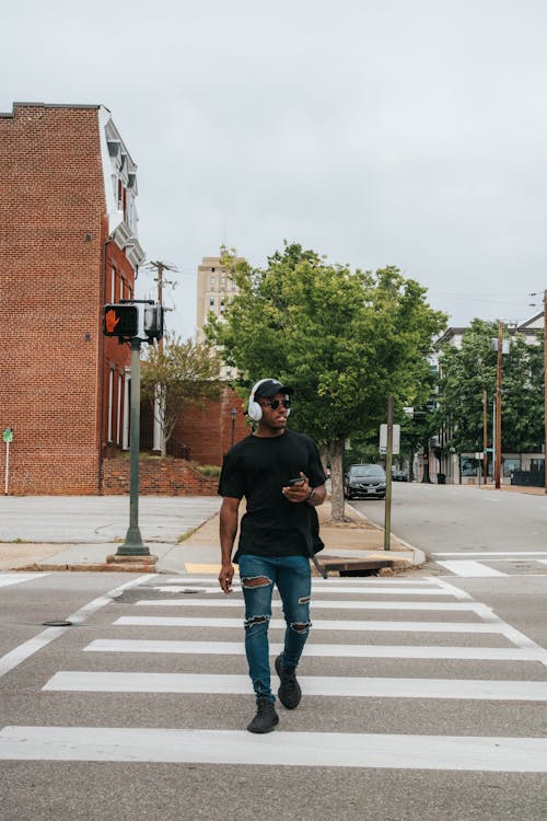 Free Man in Black Crew Neck T-shirt and Blue Denim Jeans Walking on Pedestrian Lane Stock Photo