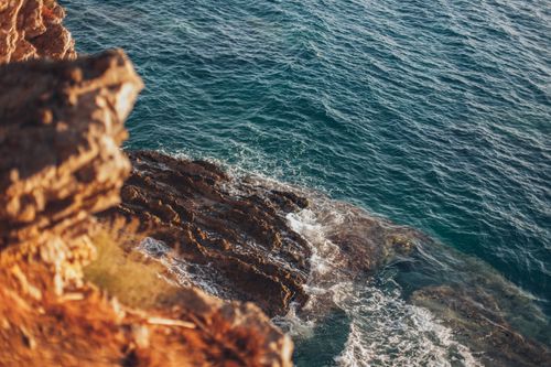 Free Captured from a high angle, waves crash against rocky cliffs with vibrant blue sea in view. Stock Photo