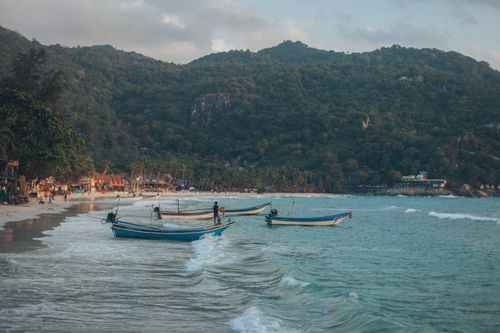 Free Panoramic view of boats by the shore against lush green hills and gentle waves under a clear sky. Stock Photo