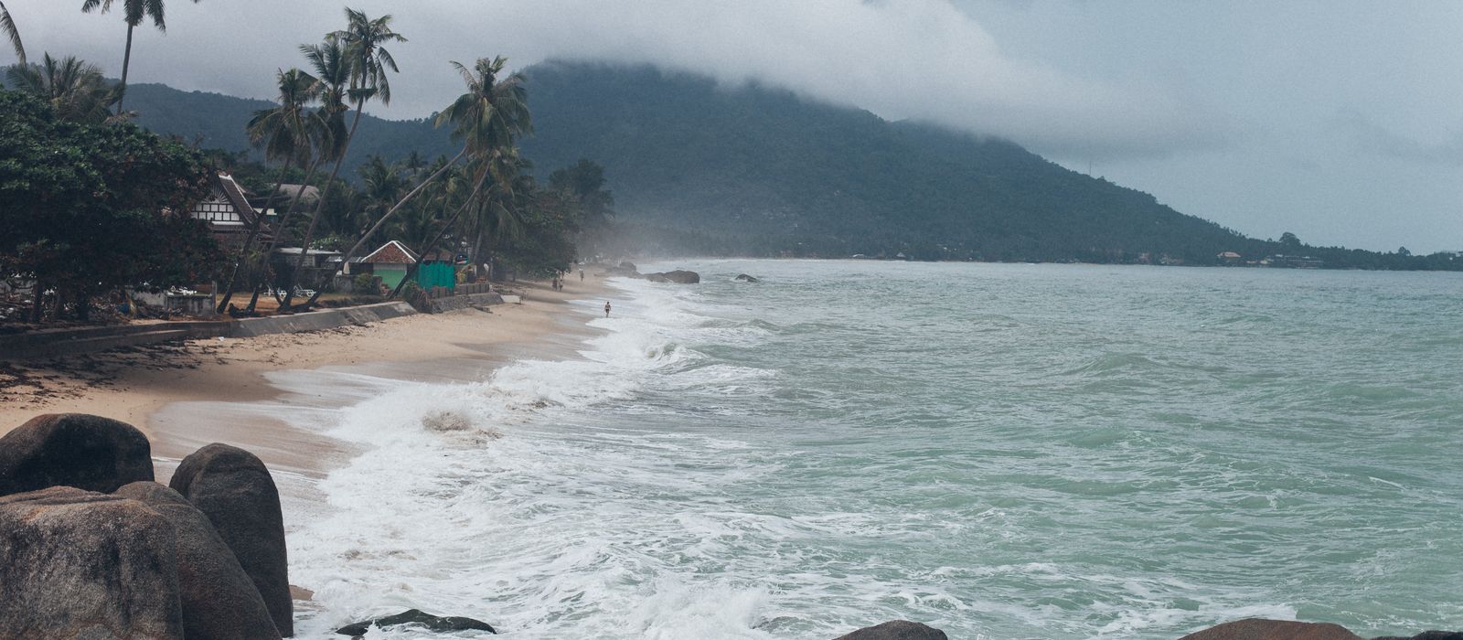 Serene view of a tropical beach in Koh Samui, Thailand, with crashing waves and lush greenery.