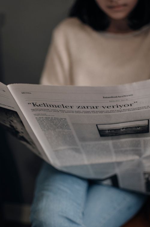 Free Unrecognizable female in casual clothes sitting on sofa and reading interesting news while spending time in living room during free time Stock Photo