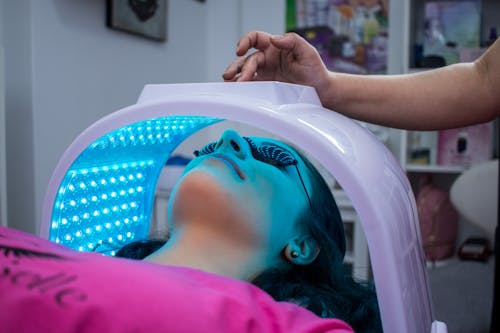Free Unrecognizable woman with dark hair with pierced ears lying under ultraviolet lamp while visiting contemporary clinic and spending time in modern salon Stock Photo