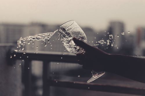 Free Unrecognizable person pouring water from glass while standing near metal fence on street with blurred buildings on background during daytime Stock Photo