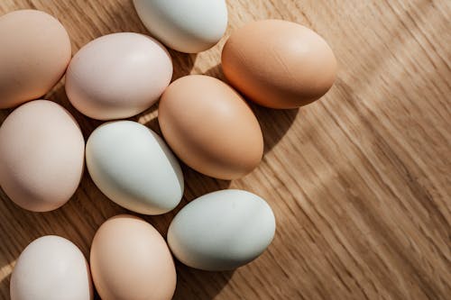 Top view of assorted mixed chicken raw multicolored eggs placed together on wooden surface during daytime